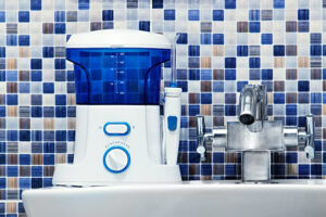 A blue and white water flosser on a bathroom sink in front of a blue, white, and gray backsplash