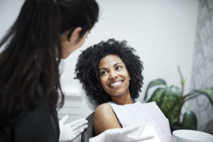 Smiling Black woman with curly hair and a white bib talks to her dentist at her routine appointment