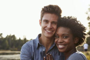 Black and white couple smile as they embrace outside in nature