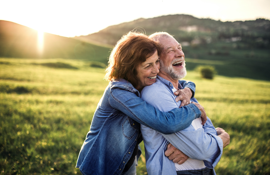 side view of senior couple hugging outside in a grassy meadow at sunset