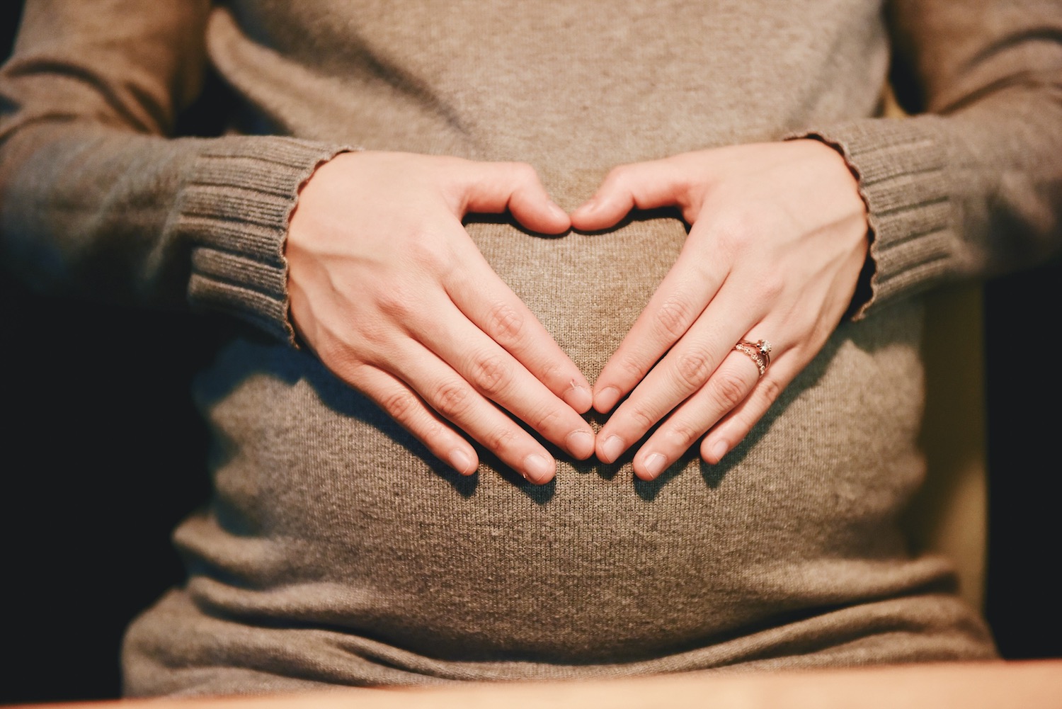 pregnancy and gingivitis, a pregnant woman in a sweater forming a heart with her hands on her belly. original public domain image from wikimedia commons