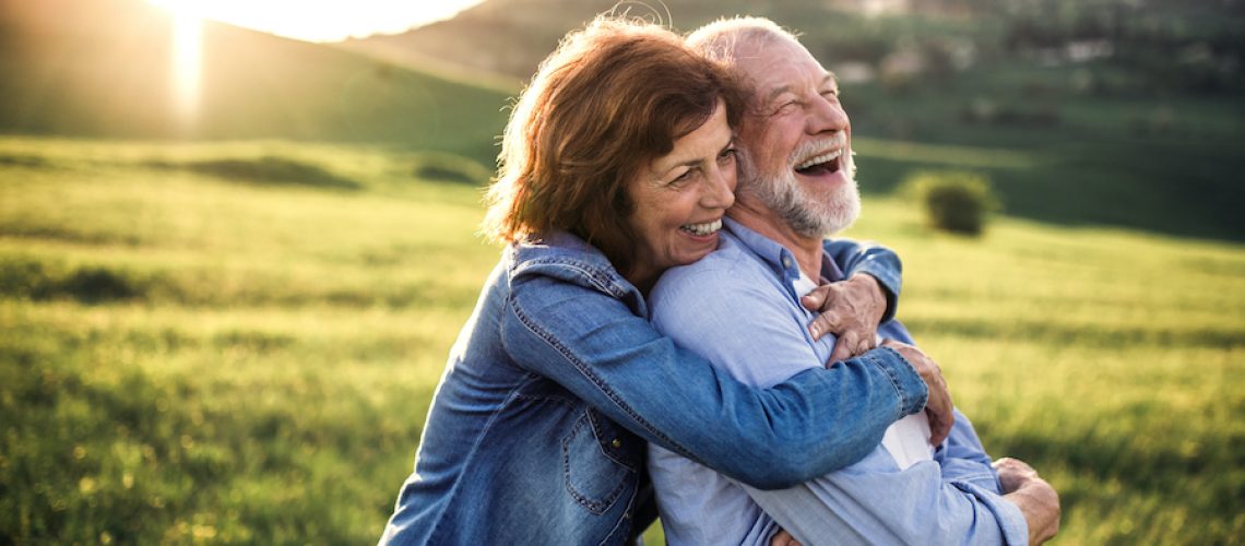 side view of senior couple hugging outside in a grassy meadow at sunset