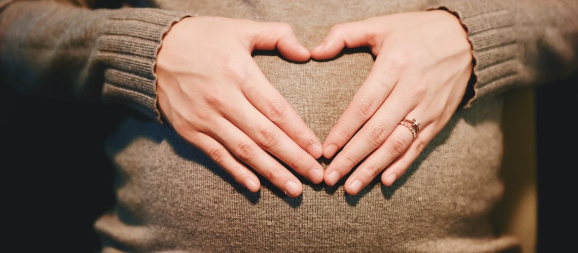 pregnancy and gingivitis, a pregnant woman in a sweater forming a heart with her hands on her belly. original public domain image from wikimedia commons