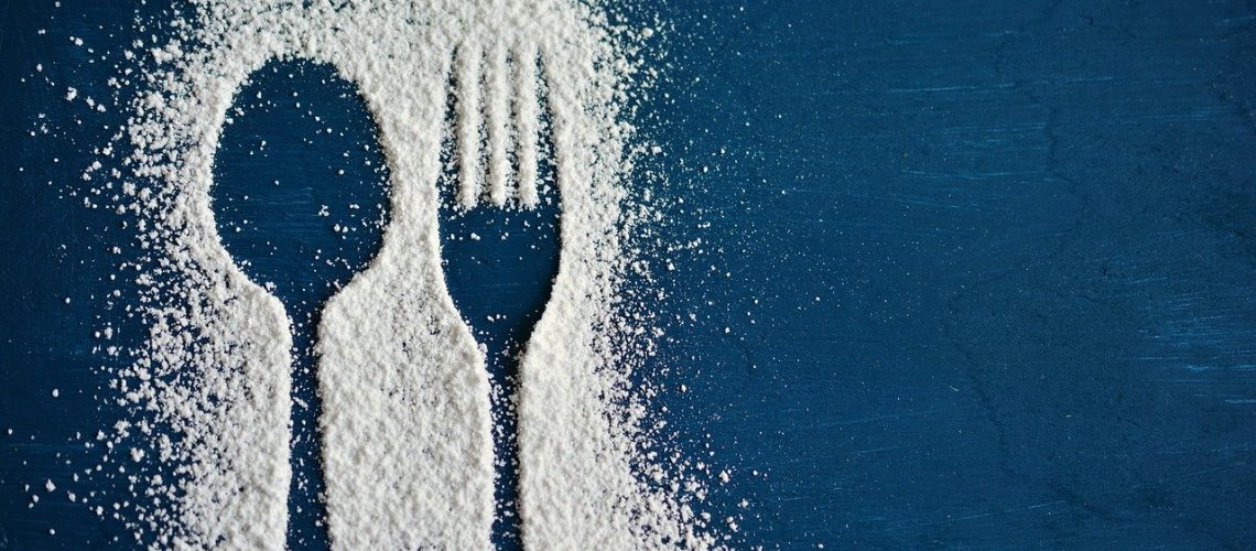 A silhouette of a spoon and fork in a sprinkling of powdered sugar on a blue table