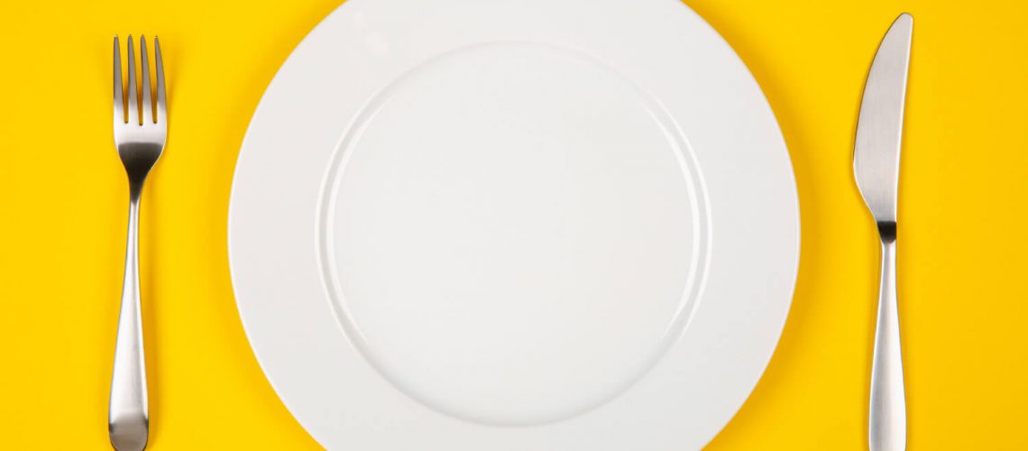 Aerial view of a white plate against a yellow table with a knife and fork